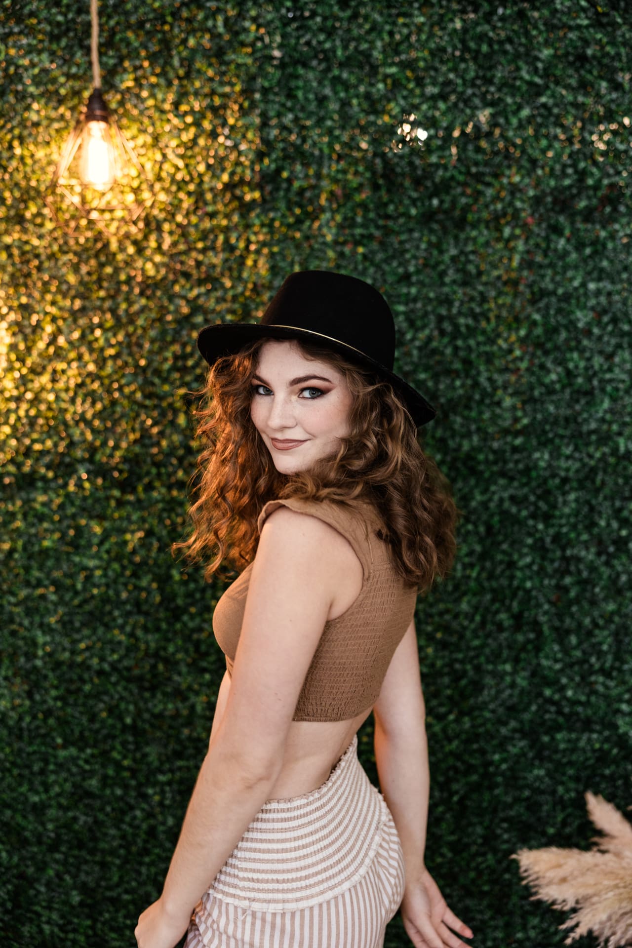 Boho model wearing floppy black hat strikes a pose in front of greenery wall during fashion photoshoot at Chicago photography studio P&M Studio