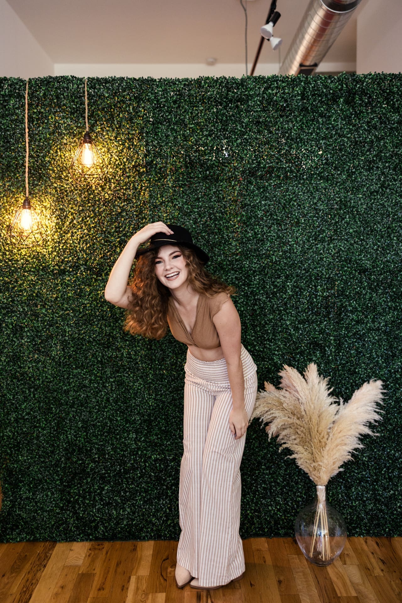Fun photo of boho model laughing in front of greenery wall with pampas grass during fashion photoshoot at Chicago photography studio P&M Studio