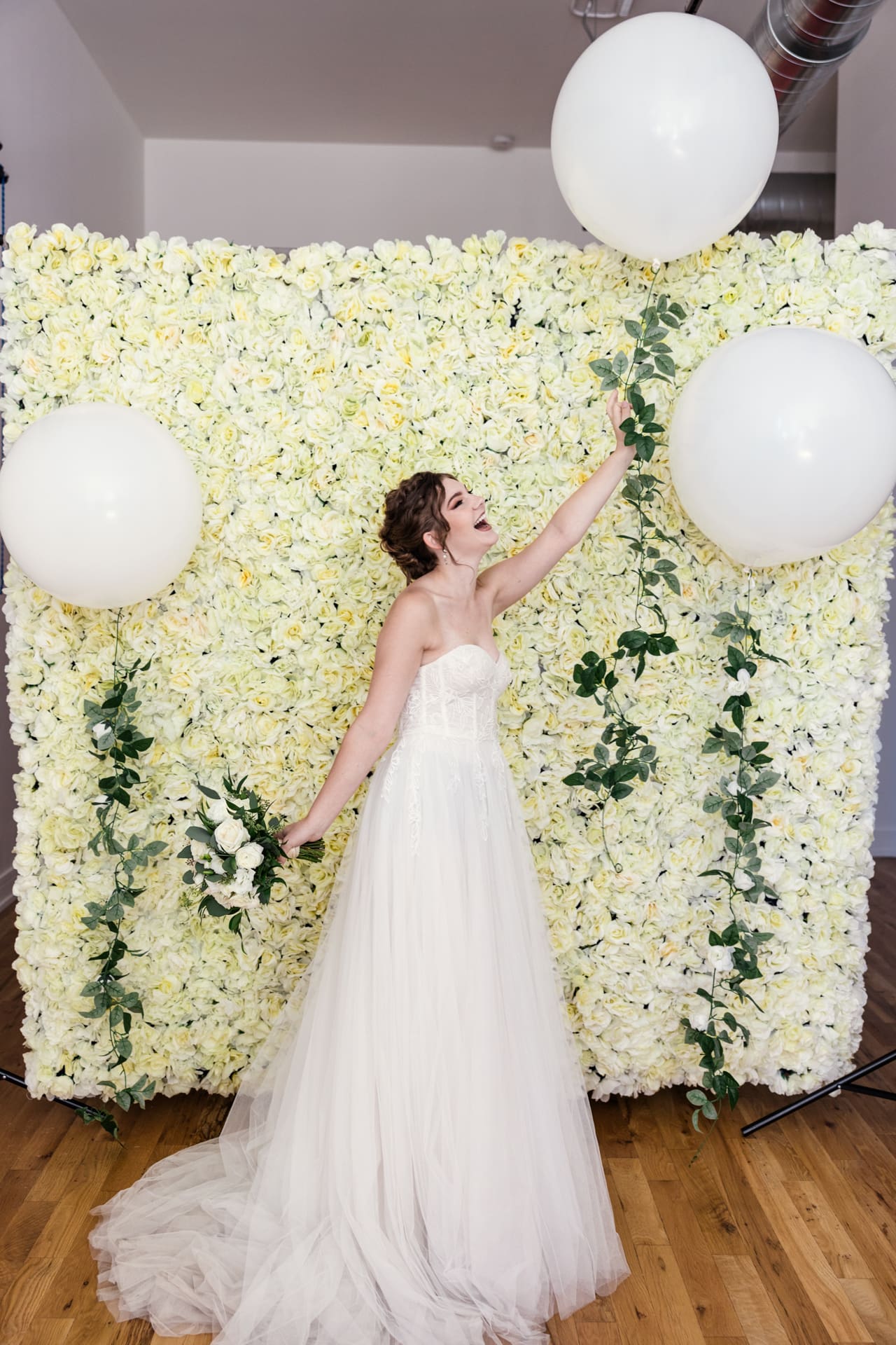 Fun portrait of bride holding giant balloon in front of white floral backdrop at Chicago photography studio P&M Studio