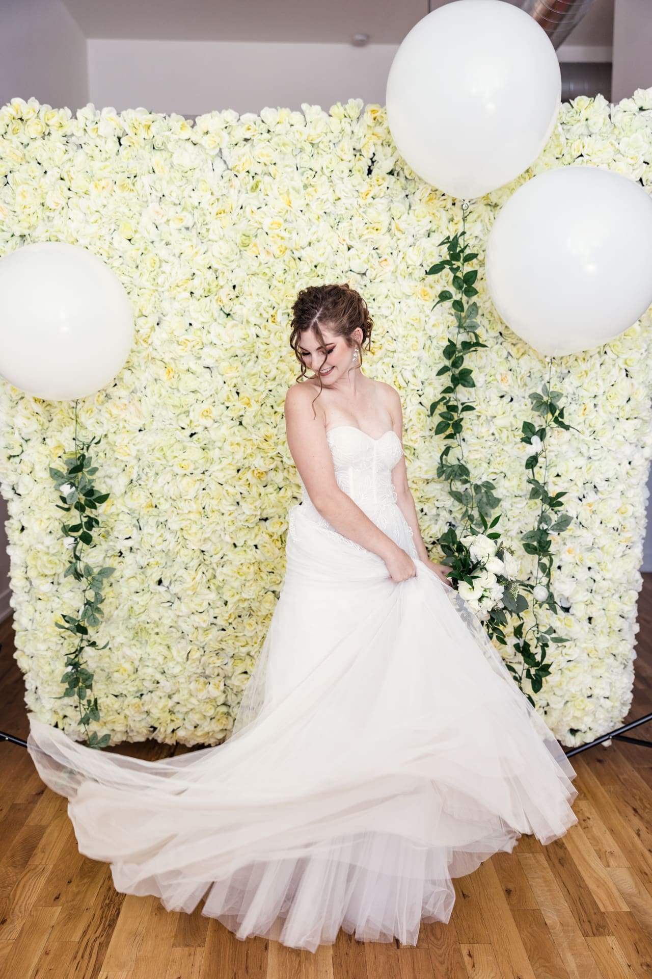 Fun portrait of bride twirling her dress with white floral backdrop and white balloons at Chicago photography studio P&M Studio