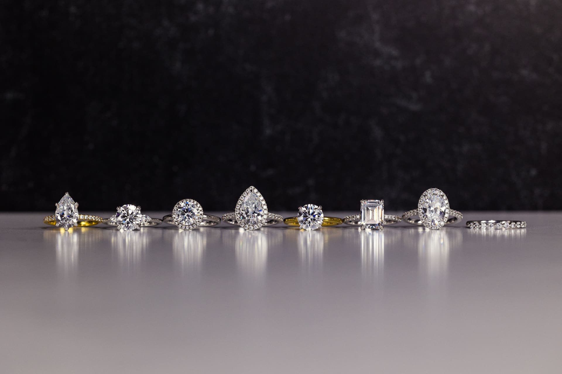 Dramatic jewelry product photography for Plum Diamonds featuring a variety of diamond ring designs on white marble counter with black background at Chicago photography studio P&M Studio