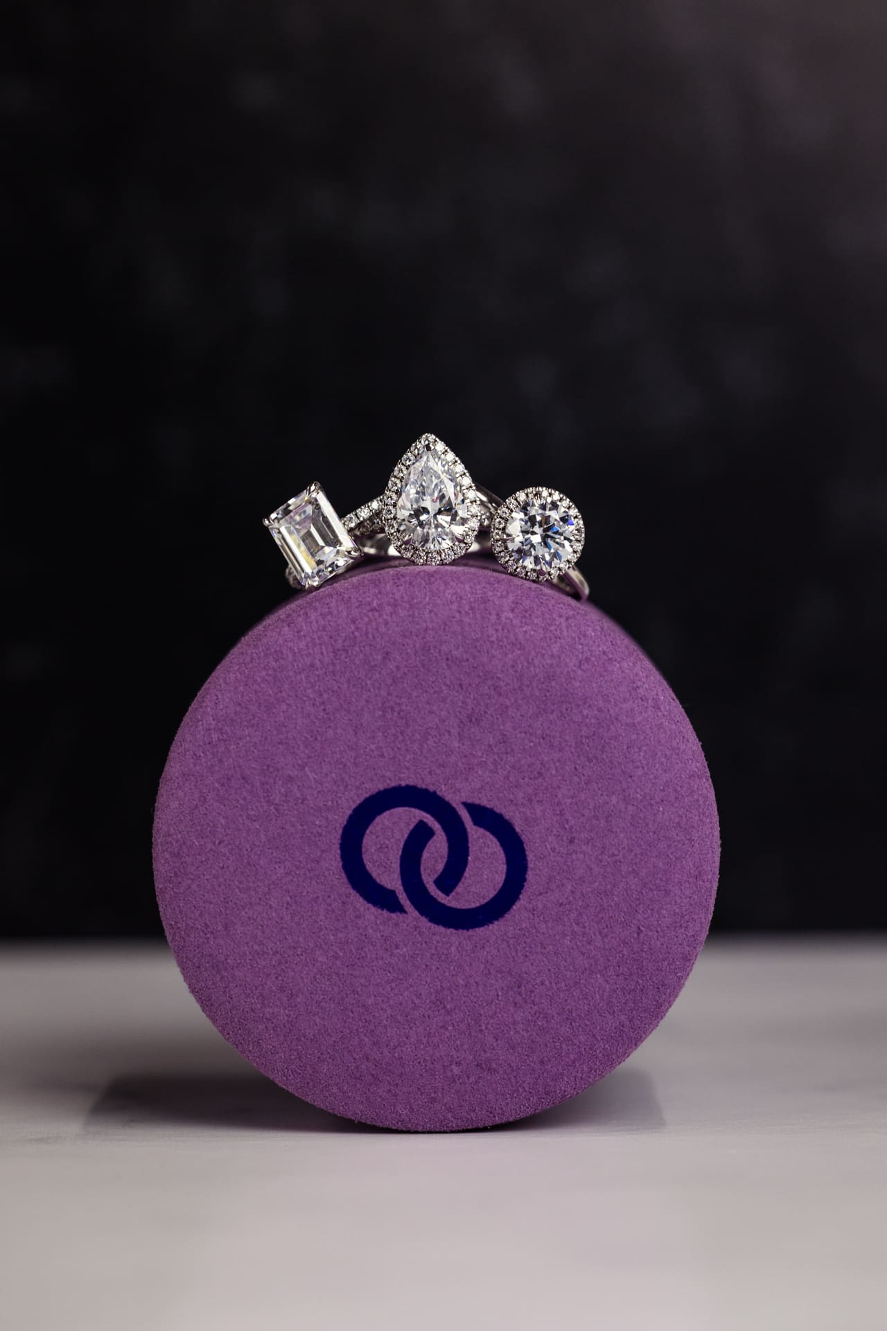 Dramatic jewelry product photo of three diamond rings sitting on purple velvet box with Plum Diamonds logo with black background at Chicago photography studio P&M Studio