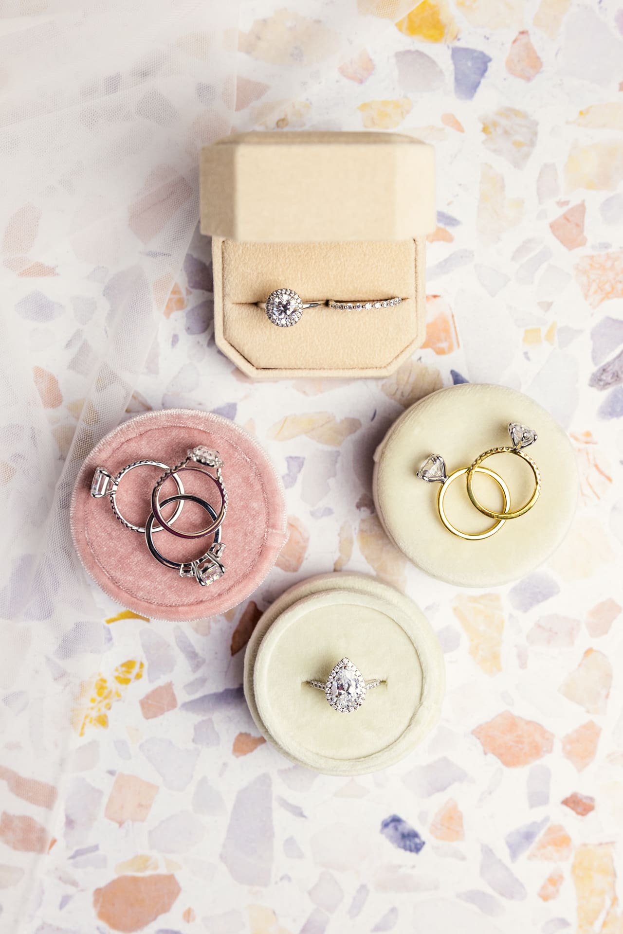 Multiple diamond engagement rings and wedding band sit on pastel ring boxes with peach, yellow and purple mosaic tile background at Chicago photography studio P&M Studio