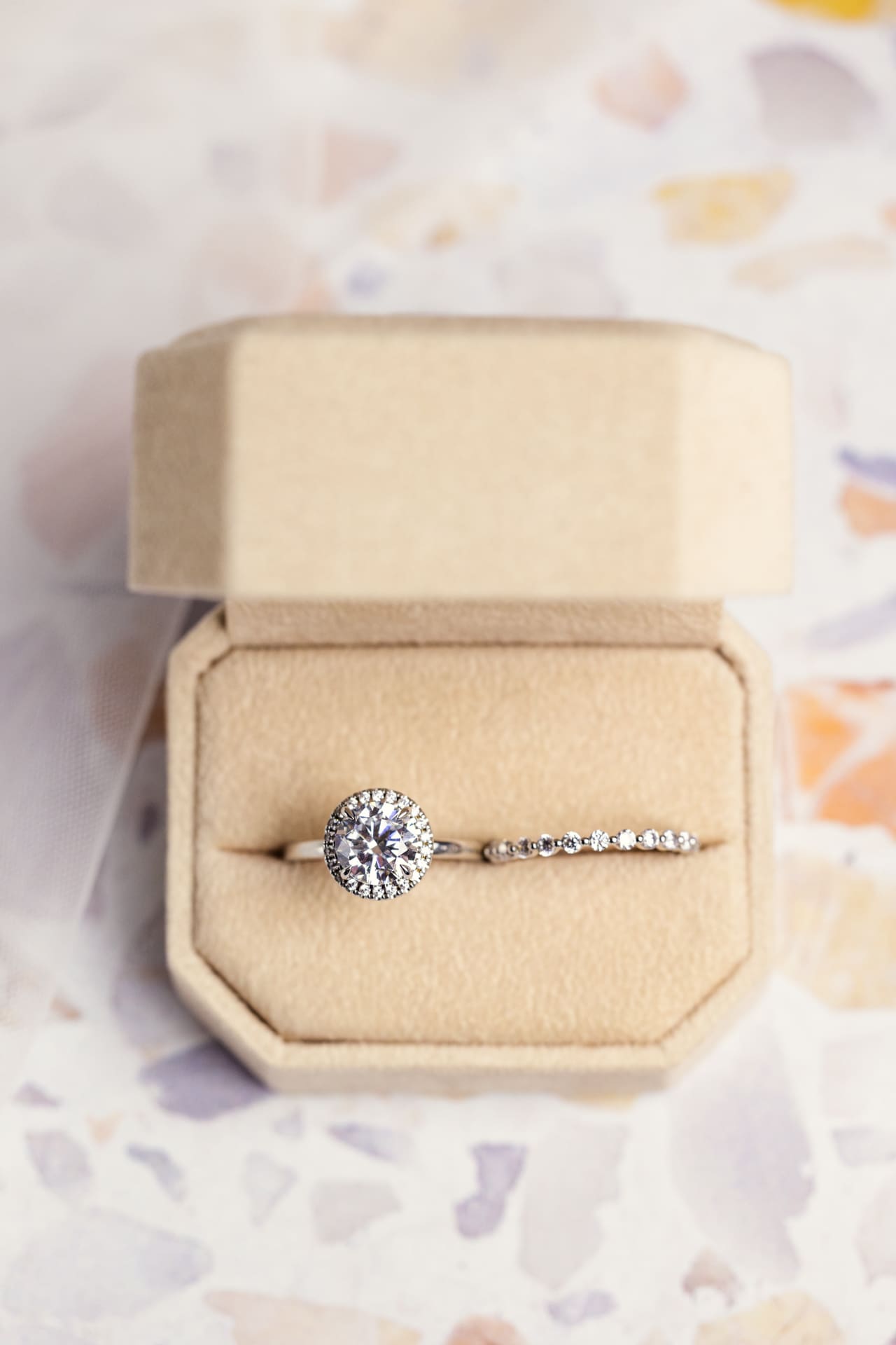 Round diamond engagement ring and diamond wedding band in peach velvet ring box on pastel mosaic counter at Chicago photography studio P&M Studio