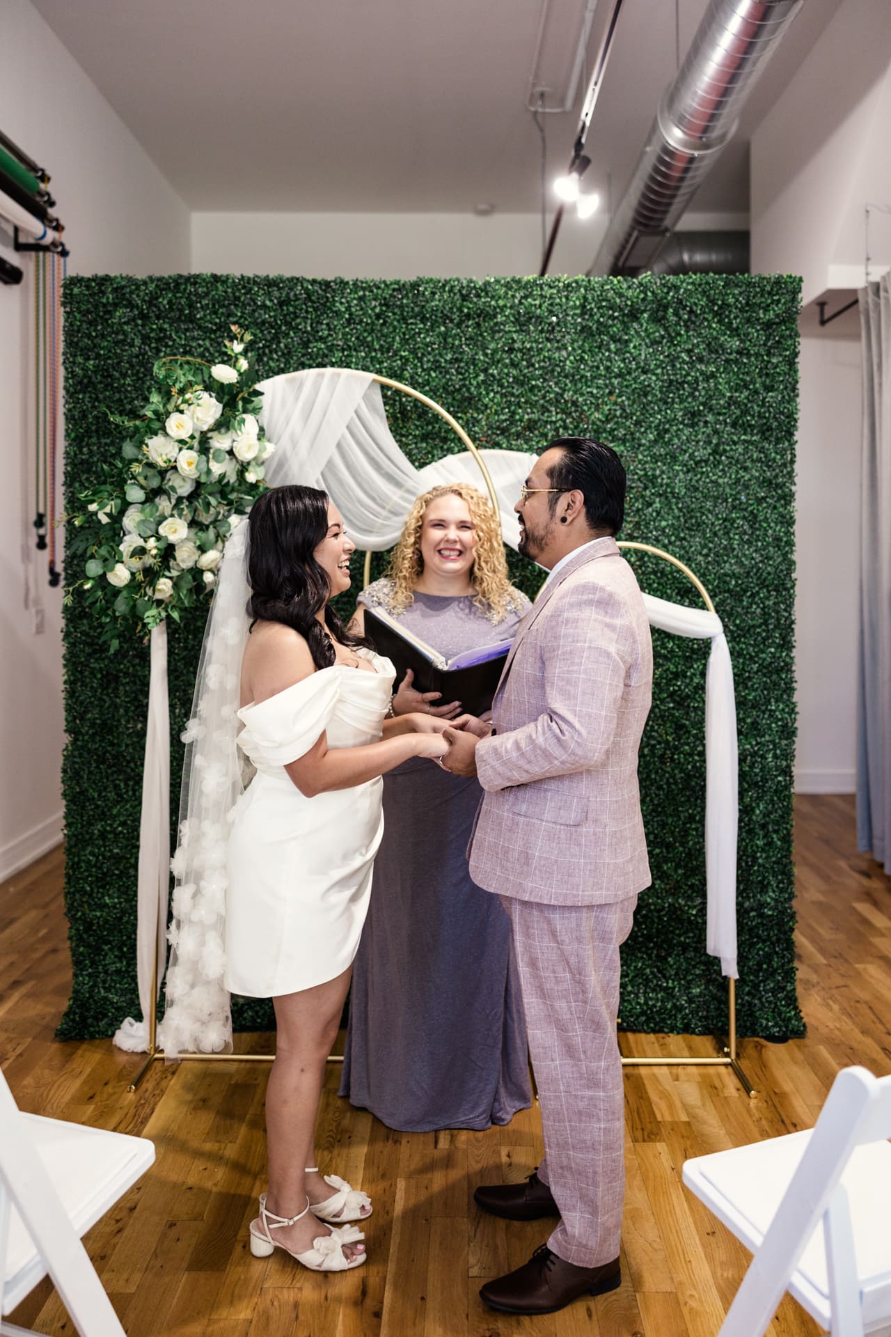 Intimate wedding ceremony in front of greenery wall with white floral decor at Chicago event space P&M Studio