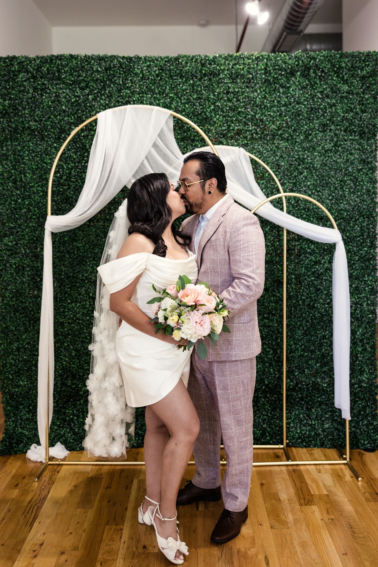 Bride and groom kiss in front of greenery wall after their intimate wedding ceremony at P&M Studio Chicago
