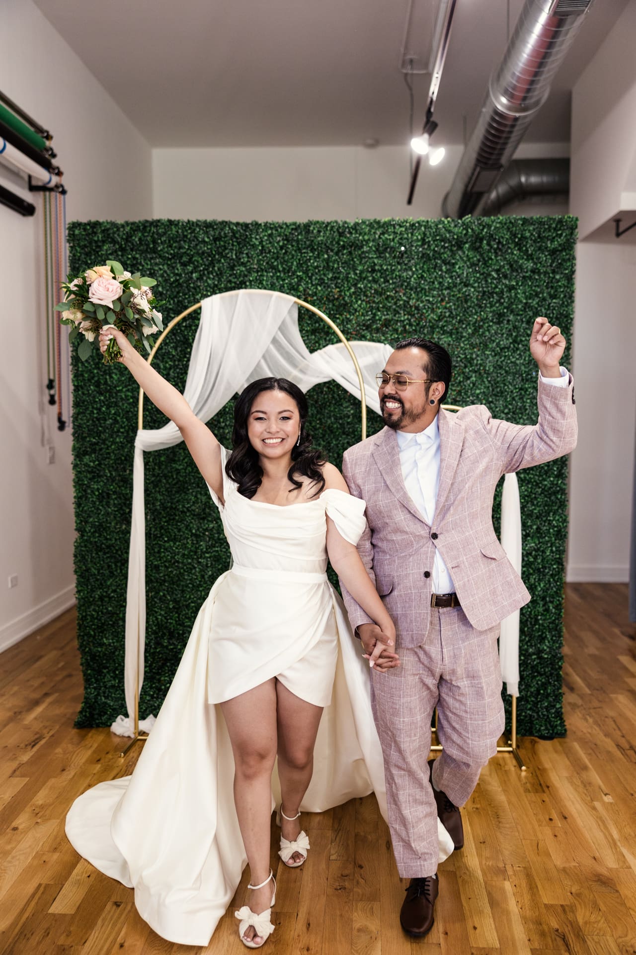 Just married bride and groom in front of gold arches and greenery wall after their intimate wedding ceremony at P&M Studio Chicago event space in West Town