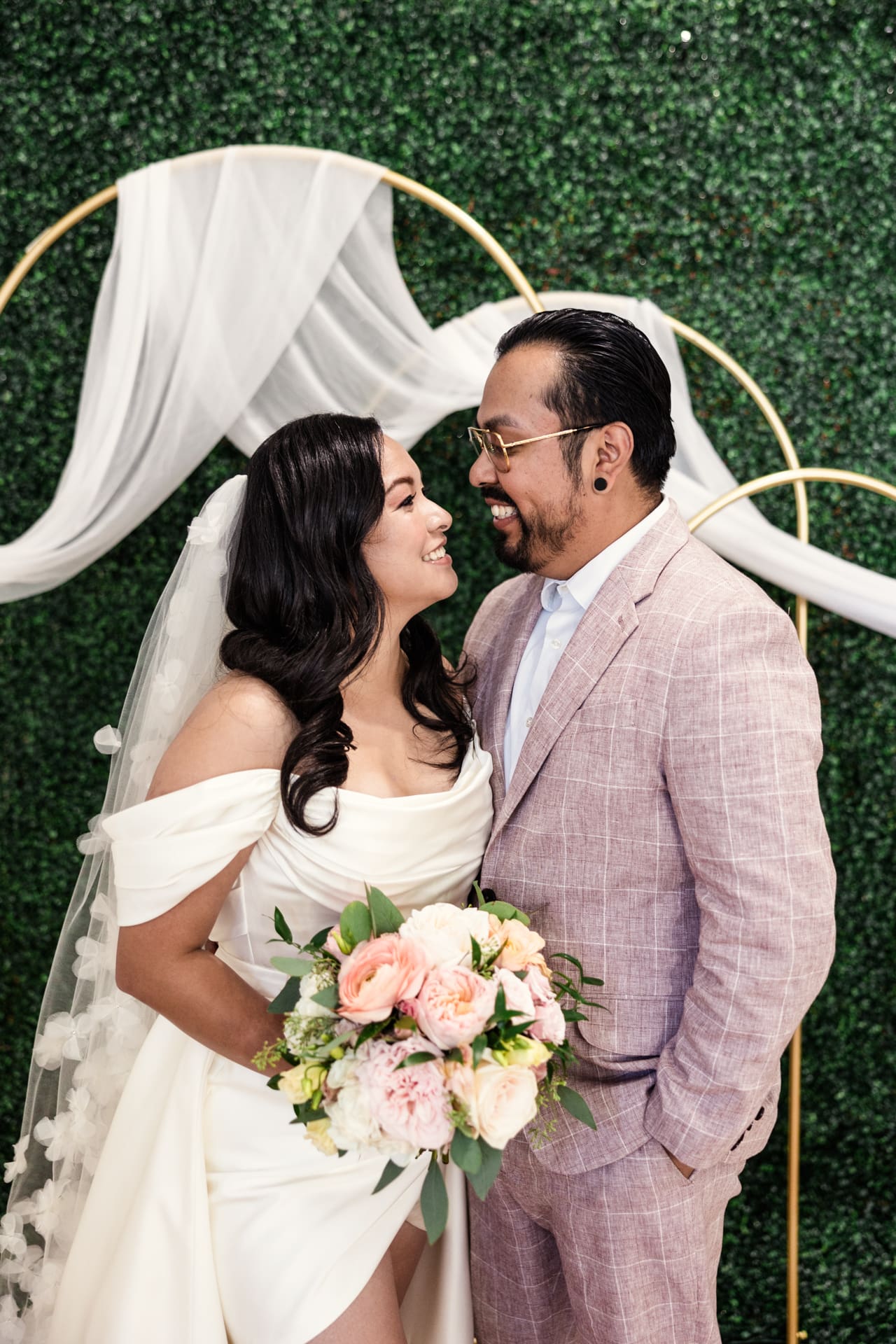 Candid photo of just married bride and groom smiling in front of gold arches and greenery wall after their intimate wedding ceremony at P&M Studio Chicago event space in West Town