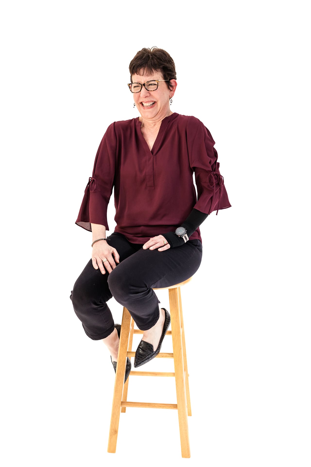 Candid studio portrait of woman laughing while sitting on stool with white backdrop at Chicago photography studio P&M Studio
