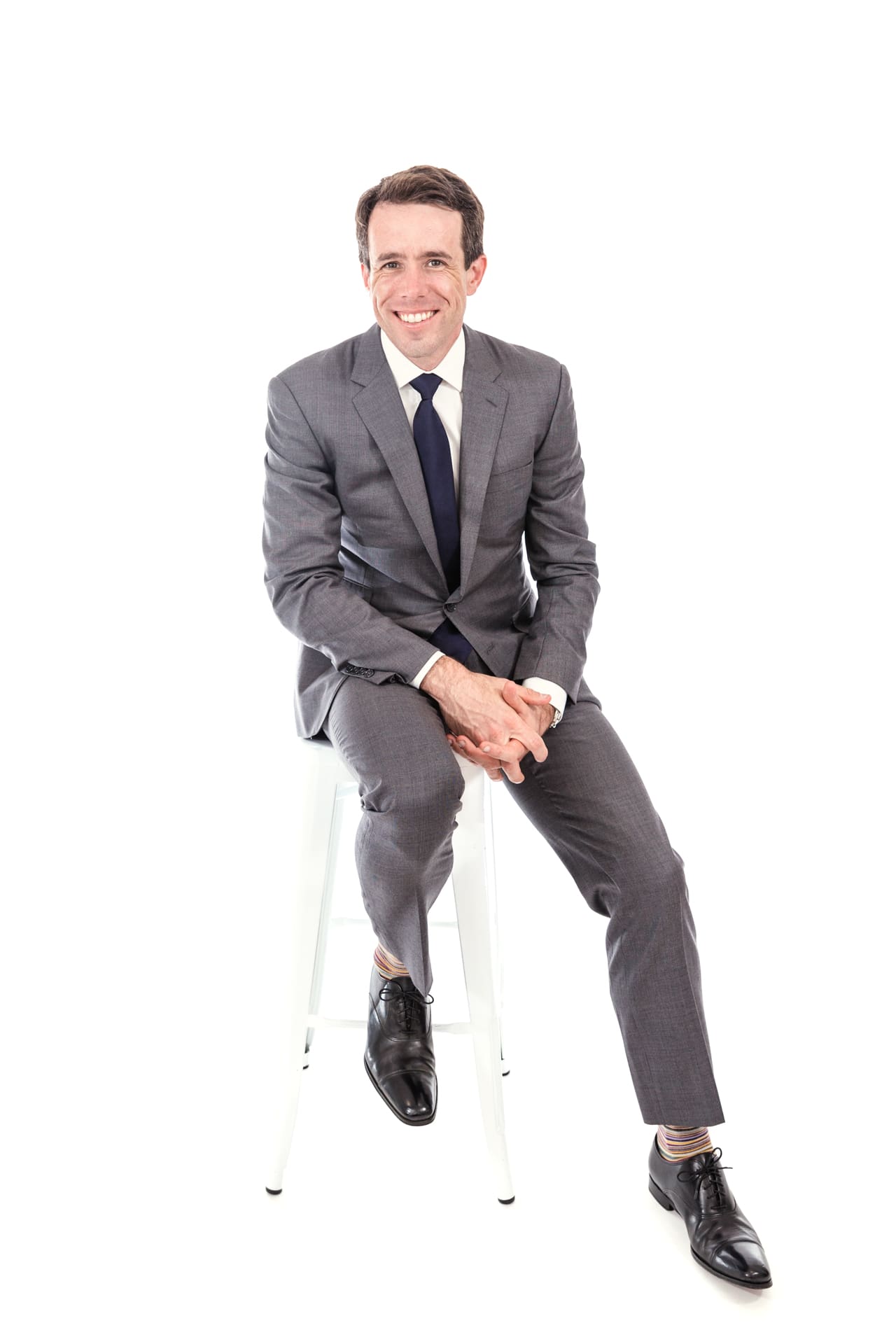 Studio portrait of man in gray suit and blue tie sitting on stool with white backdrop at Chicago photography studio P&M Studio